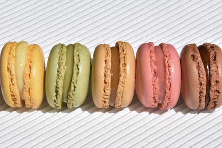 Five macarons of different flavor ordered in a row on a white relief striped background. Macro view