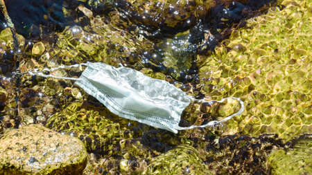 Used face mask contaminating the transparent waters of a mountain stream. Environmental concern...