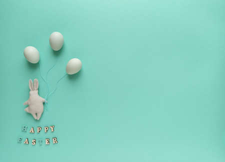 Easter holiday concept, flat layout, top view. Colorful Easter eggs on a turquoise background. A small gray rabbit made of cloth.の写真素材