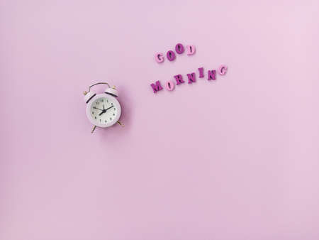 The concept of awakening. A white alarm clock on a pink background with a good morning wish.の写真素材