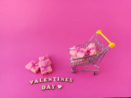 Buying gifts via the Internet. A small metal trolley on a pink background with gifts on a pink...