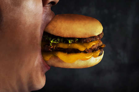 Young man eating cheese burgerの写真素材