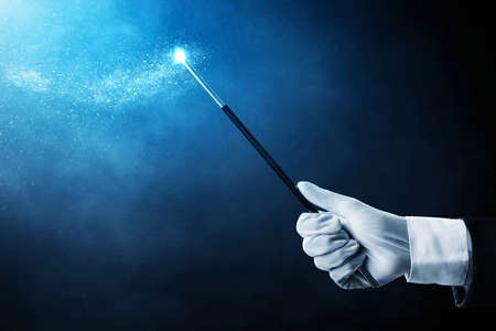 Magician hand holding magic wand on dark background