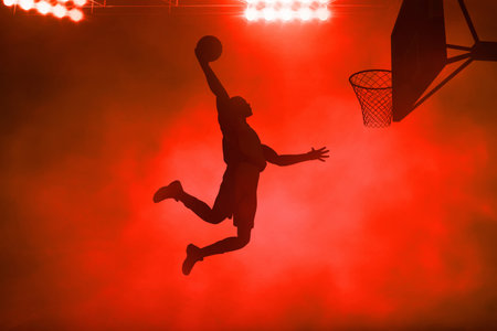 3d illustration shadow silhouette of young professional basketball player slam dunk on dark red smoke backgroundの写真素材