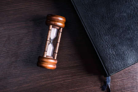 Hourglass and the book on wood background.