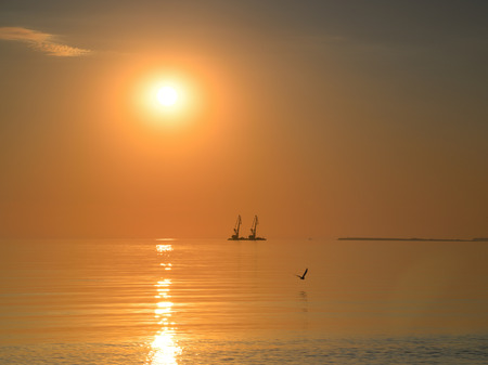 two large offshore floating cranes on the horizon at sunset produce their workの写真素材