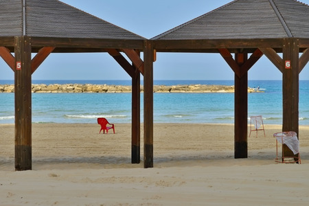 the beach in the morning the Israel Mediterranean sea the beginning of the season clean shore a lone red chair and gazebos from the sun against the blue sky and breakwaterのeditorial素材