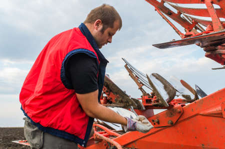 Young mechanic fixing plow on the tractor