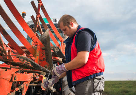 Young mechanic fixing plow on the tractorの写真素材