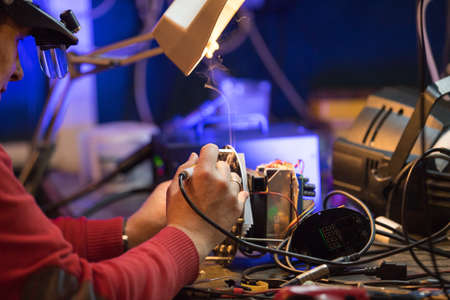Young man with safety glasses repairing motheboard with soldering ironの写真素材