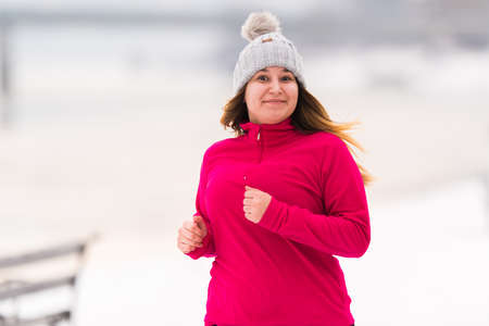 Pretty girl wearing sportswear and running on snow during winterの写真素材