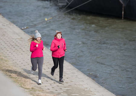 Mother and daughter wearing sportswear and running on windy day at quayの写真素材
