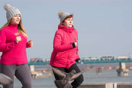 Mother and daughter wearing sportswear and running on windy day at quay