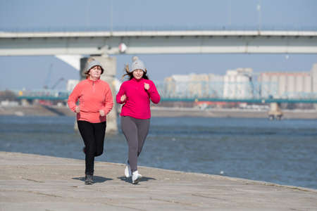 Mother and daughter wearing sportswear and running on windy day at quayの写真素材