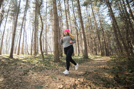 Pretty girl wearing sportswear and running in forest at mountain during winterの写真素材