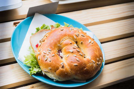 Fresh bun sandwich with ham, cheese, bacon, tomatoes, lettuce, cucumbers on light wooden table at window shopsの写真素材