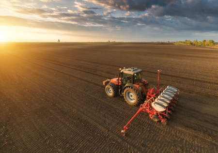 Farmer with tractor seeding - sowing crops at agricultural fields in springの写真素材