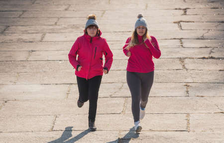 Mother and daughter wearing sportswear and running on windy day at quay