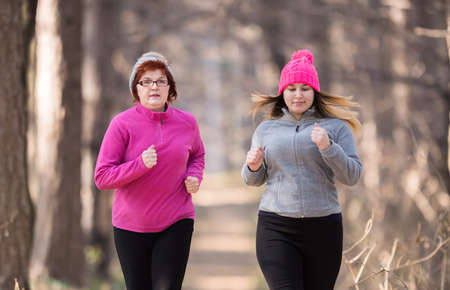 Mother and daughter wearing sportswear and running in forest at mountain during winterの写真素材