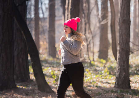 Pretty girl wearing sportswear and running in forest at mountain during winter