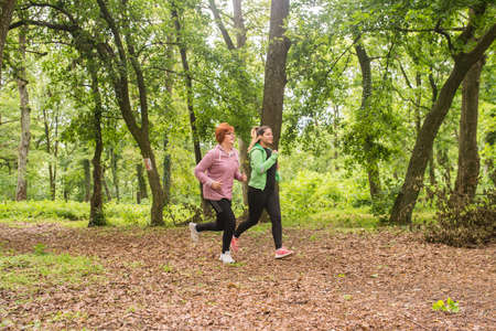 Mother and daughter wearing sportswear and running in green forest at mountainduring springの写真素材