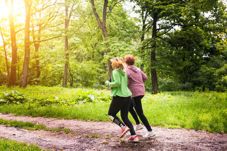 Mother and daughter wearing sportswear and running in green forest at mountainduring springの写真素材