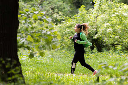 Pretty girl wearing sportswear and running in green forest at mountainduring spring