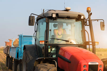 Beautiful, young farmer girl is driving tractor at field