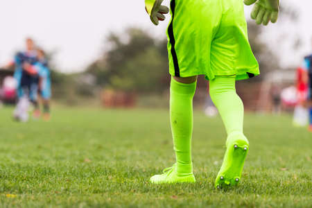 Kids soccer football - little goalkeeper in green goalkeeper jersey at soccer field with matching glovesの写真素材