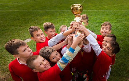 Kids soccer football - young children players celebrating with a trophy after match on soccer fieldの写真素材