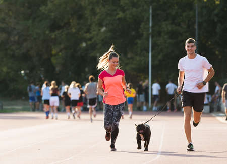 Young couple runnig with french bulldog  at sport field の写真素材