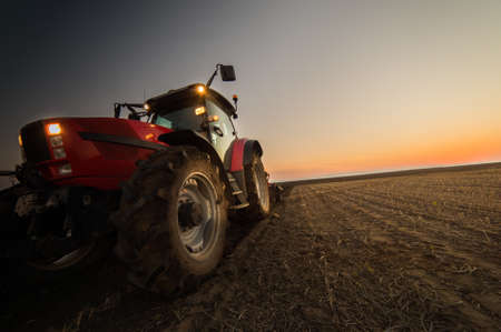 Tractor plowing plow the field on a background sunset.の写真素材