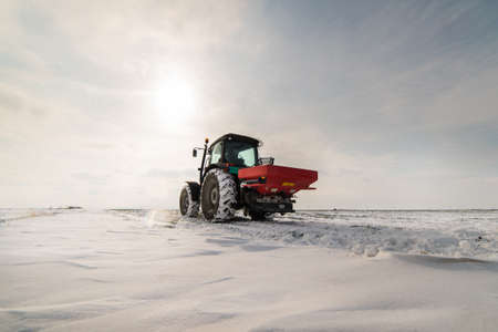 Farmer with tractor seeding - sowing crops at agricultural fields in winter - snowの写真素材