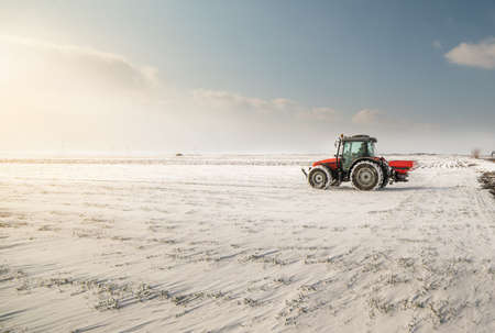 Farmer with tractor seeding - sowing crops at agricultural fields in winter - snowの写真素材