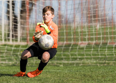 Young Boy Goalkeeper Saving A Football In A Game Of Soccer.の写真素材