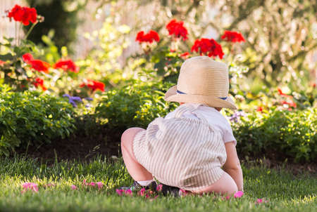 Baby boy sitting on the grass  watching flowers in the garden on beautiful spring dayの写真素材