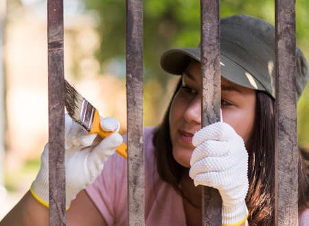 Pretty girl is painting wooden fence with a brushの写真素材