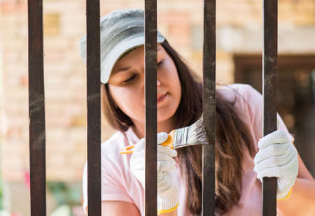 Pretty girl is painting wooden fence with a brushの写真素材