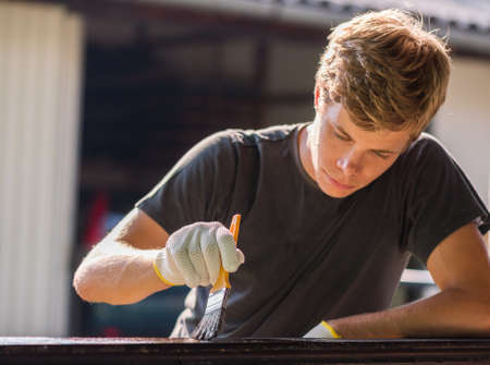 Young handsome man is painting wooden fence with a brush