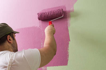 Young man is painting wall with painting rollerの写真素材