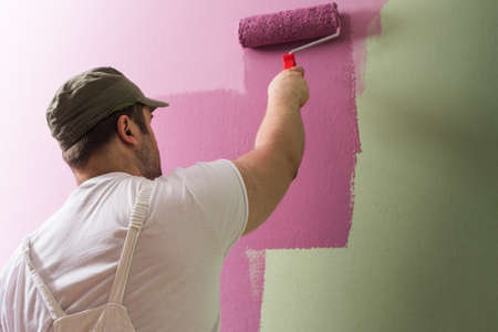Young man is painting wall with painting rollerの写真素材