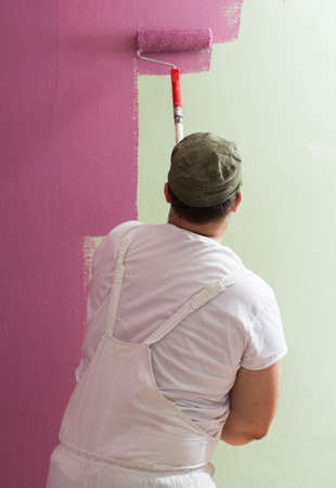 Young man is painting wall with painting rollerの写真素材