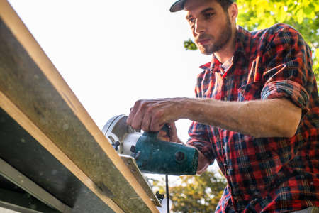 Carpenter using circular saw cutting wooden boards with hand power tools.の写真素材