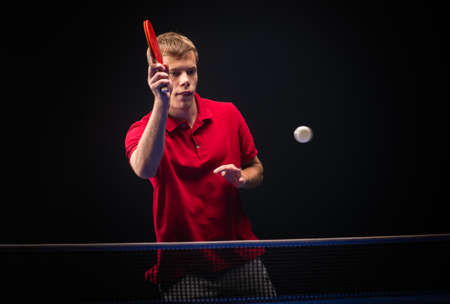 Young man playing table tennis on black studio background.