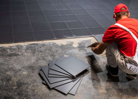 A construction worker putting on new floor tiles.