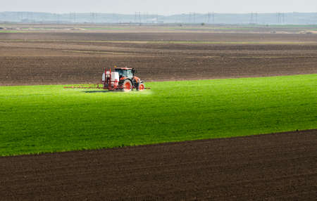 Tractor spraying pesticides over a green field