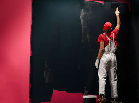 Man painting a wall. Painter in red overall painting wall in black colorの写真素材