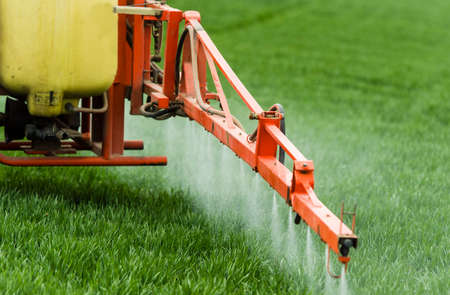 Tractor spraying pesticides over a green fieldの写真素材