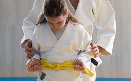 Experienced judo trainer with black belt tying belt for his pupil before competitionの写真素材