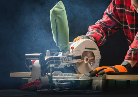 Closeup of young man sawing lumber with sliding compound miter saw indoors.の写真素材